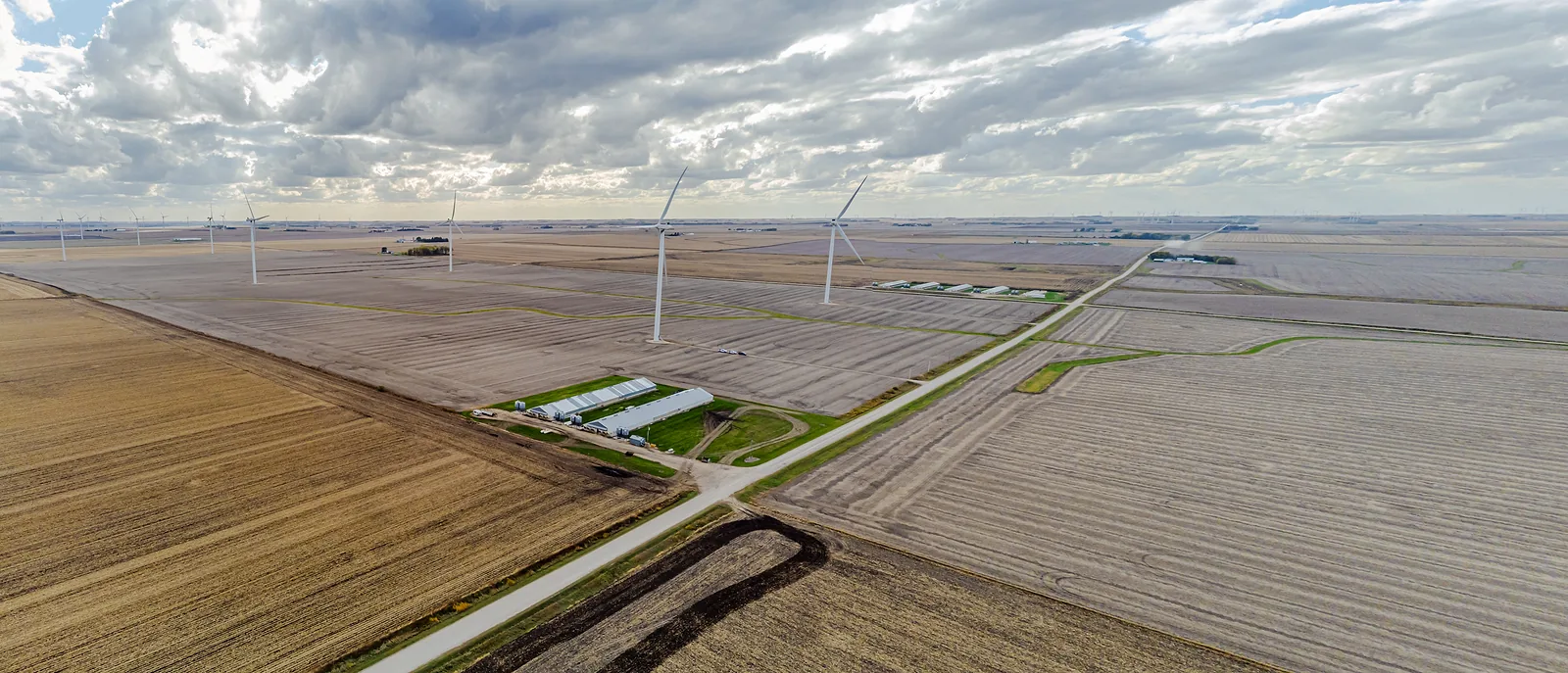 Flat farmland seen from the air, with a few wind turbines and a road running to the horizon.