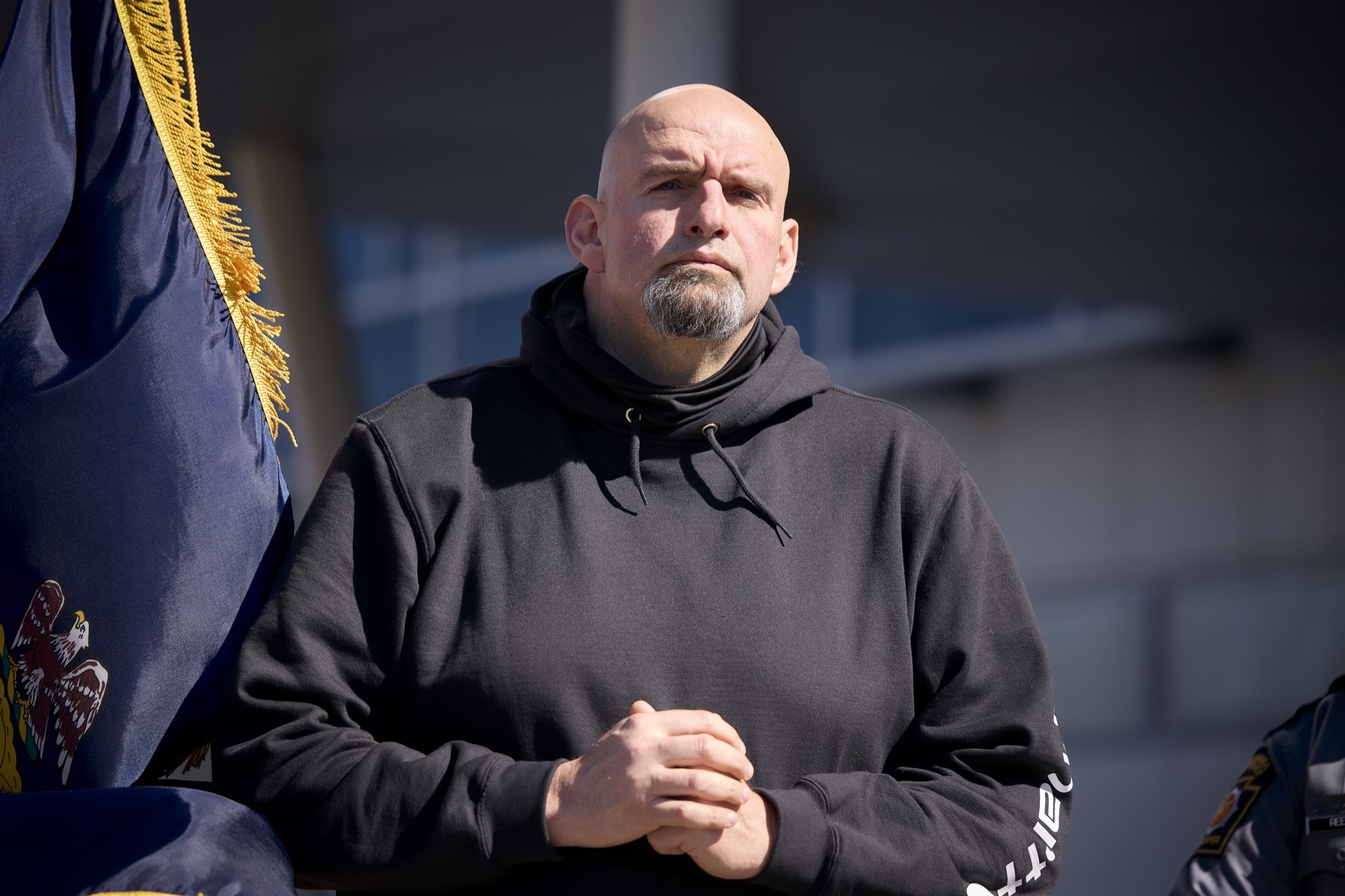 John Fetterman in a black hooded sweatshirt beside a Pennsylvania flag, March 2022.